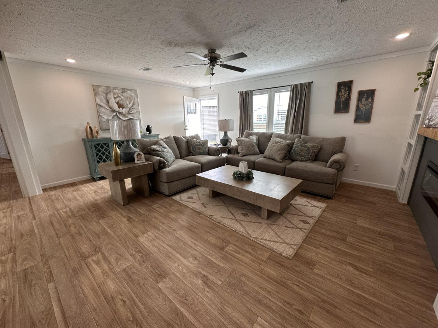 Luxury modern manufactured home showcase of the APH 1662C and expansive double-wide models, featuring charcoal horizontal siding with rustic wood shutters and white board-and-batten farmhouse exteriors. High-end interiors highlight open-concept living rooms with integrated electric fireplaces and shiplap accent walls, gourmet kitchens with large marble-look islands and custom pull-out pantry storage drawers, vaulted shiplap ceilings with dark wood beams, and cozy bedrooms featuring modern white iron frames and neutral-toned decor. Concluding with a spacious covered front porch featuring a dark wood-plank ceiling and a stylish hanging wicker egg chair.