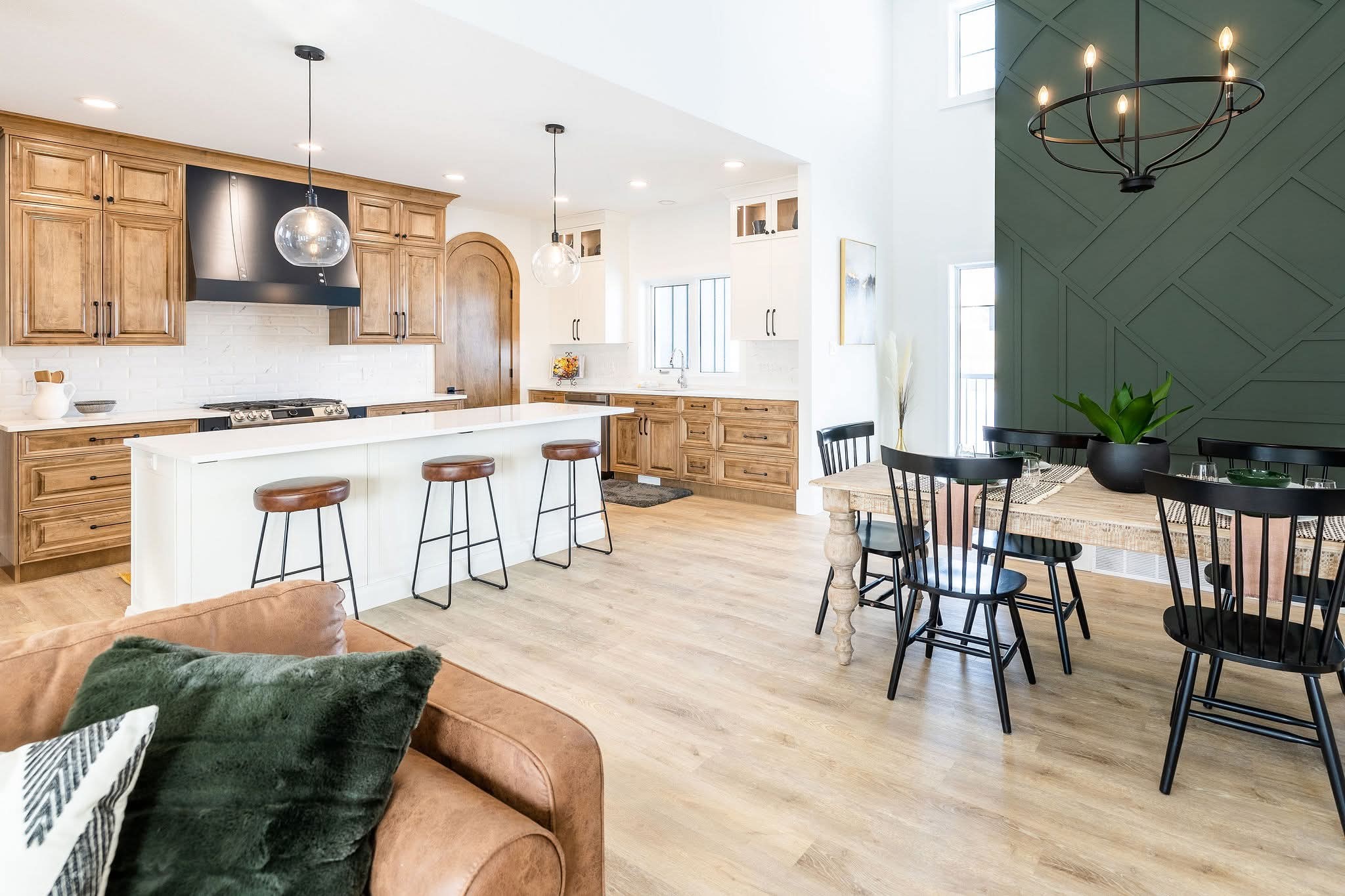 Modern kitchen and dining area with warm wood cabinets, a large white island, pendant lights, and a rustic dining table. Cozy, inviting atmosphere.