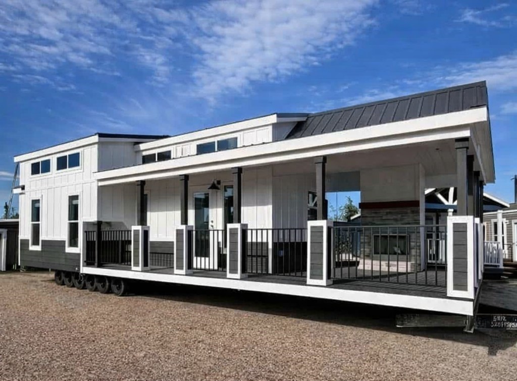 Modern tiny home on wheels with a white and black exterior, large windows, and a covered porch. Set against a bright blue sky, exuding a serene, minimalist vibe.