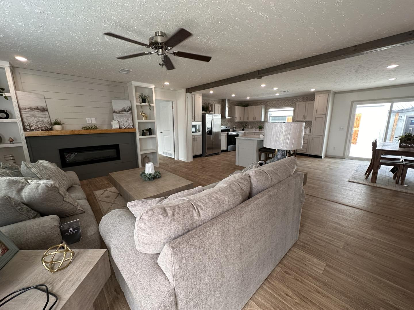 Modern modular home showcase featuring the APH 1662C 819 SQ FT show home and large double-wide models, with white vertical board and batten siding, dark grey horizontal siding with wood shutters, luxury interiors featuring vaulted shiplap ceilings with dark wood beams, gourmet kitchens with granite islands and custom pull-out pantry storage, open-concept living rooms with stacked stone and shiplap fireplaces, and cozy bedrooms with modern white iron or upholstered bed frames and dark-trimmed windows.