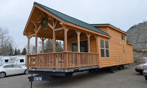 To maximize your website’s search engine rankings and ensure accessibility, here is a comprehensive Ultra-Level SEO Alt Text description for this gallery of luxury manufactured homes, park models, and tiny homes. Ultra-Level SEO Alt Text High-end housing showcase featuring a diverse collection of modern manufactured homes, tiny homes, and park models, including the expansive "The Boujee XL" aesthetic. Exterior Architectural Styles: Highlights include classic white and sage green board-and-batten tiny homes with grand pillared front porches, black metal railings, and gabled roofs. A standout premium model features a striking dark charcoal exterior with a copper-tone metal roof, natural cedar wood accents, and a large wrap-around elevated wooden deck. Also featured is a spacious tan manufactured home with decorative red shutters and a full-length covered porch. Interior Living & Custom Design: Open-concept interiors are defined by high-fidelity finishes, including vaulted ceilings with rustic dark wood beams or light natural wood planks and white shiplap walls. Living areas showcase a "modern boujee" style with integrated electric fireplaces, neutral-toned sofas, and lofted sleeping quarters with black metal balustrades. Rustic cabin-style interiors feature all-over natural wood walls, complemented by modern navy blue cabinetry and industrial-style black ceiling fans. Gourmet Kitchens & Dining: The collection features diverse kitchen layouts, ranging from cozy rustic cabin kitchens to expansive modern designs. High-end features include oversized kitchen islands, marble-look or dark stone countertops, farmhouse-style cabinetry in navy or white, and professional-grade stainless steel appliances. Modern lighting includes elegant pendant chandeliers and recessed LED fixtures. Spa-Inspired Bathrooms & Master Suites: Bathrooms emphasize modern luxury with walk-in tile showers featuring marble-look surrounds, black matte hardware, and contemporary grey vanities with ample storage. Master bedrooms offer clean, minimalist designs with neutral carpeting and large windows for natural light. This gallery represents the pinnacle of "boujee" manufactured living, combining versatile floor plans with sophisticated modern farmhouse aesthetics.