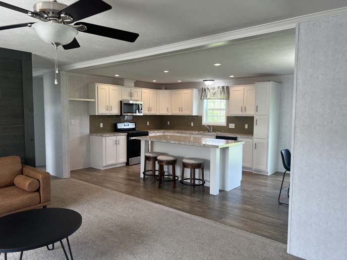 Modern manufactured home exterior with grey siding, black shutters, and white trim on a gravel lot.