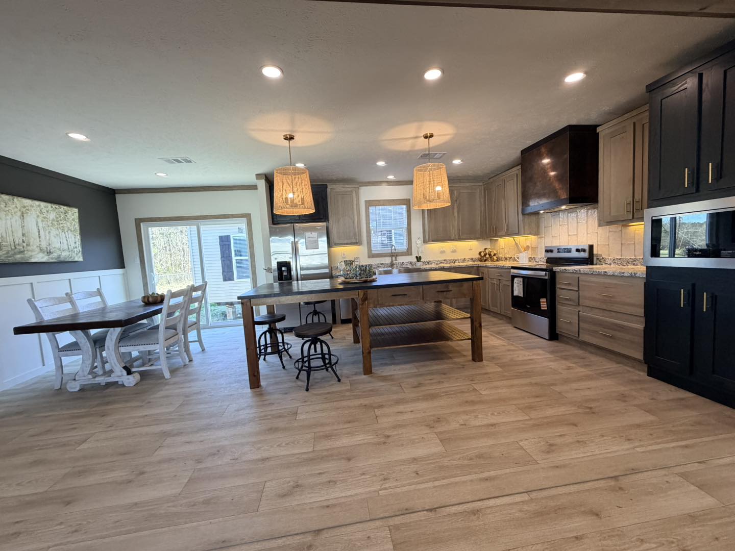 Spacious kitchen with wood flooring, featuring a large island with stools, pendant lights, and modern appliances. Adjacent dining area with a table and chairs. Warm and inviting ambiance.