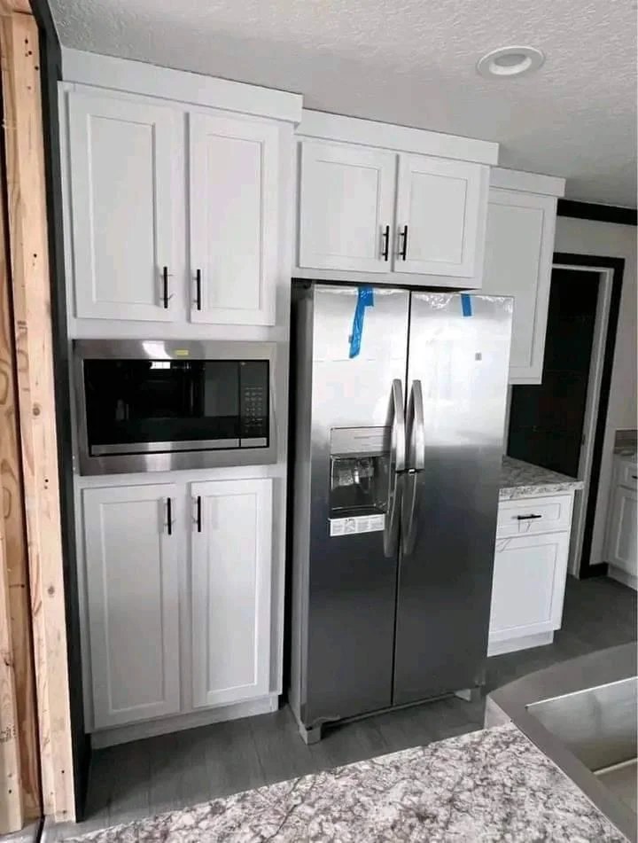 Modern kitchen with white cabinets, a built-in microwave, and a stainless steel fridge. Gray granite countertop adds a sleek look.