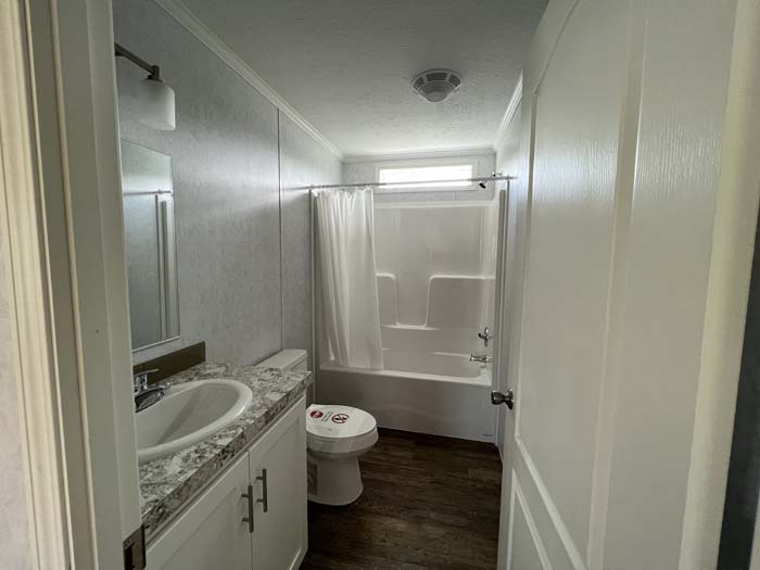 Clean guest bathroom in a manufactured home featuring a white vanity with marble-style countertop and a standard tub-shower combo.