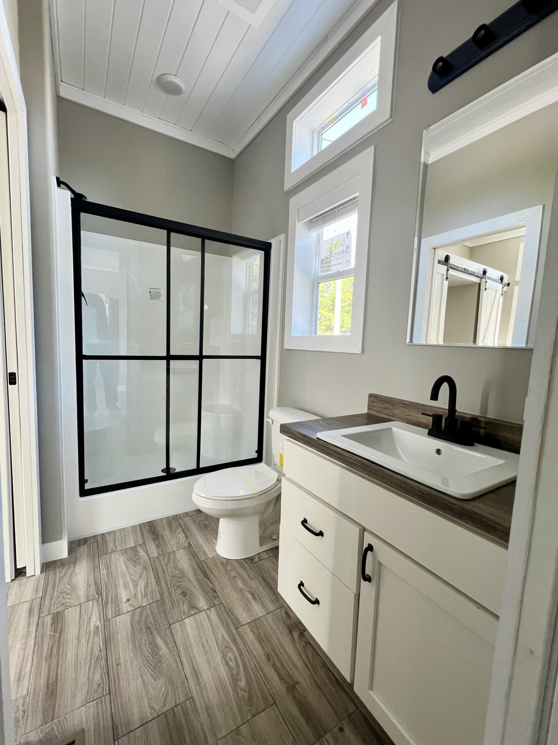 Modern bathroom with a large shower enclosed by black-framed glass, a toilet, and a white vanity with a black faucet. The space feels bright and clean.