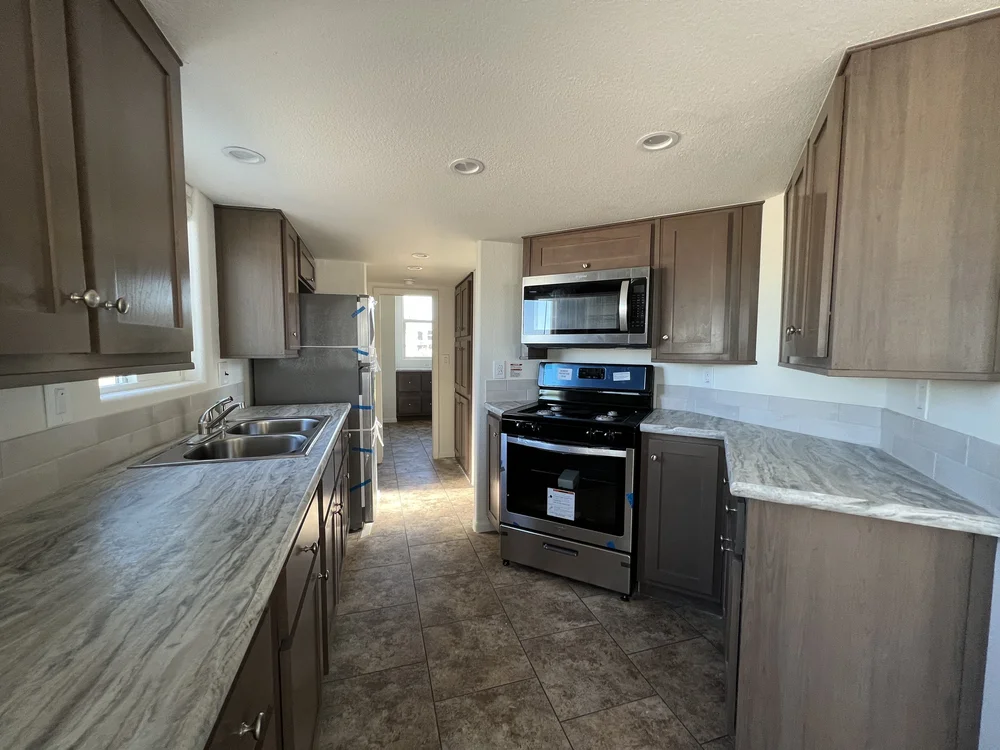 Modern kitchen with brown cabinets, marble countertops, and stainless steel appliances. Sunlight streams through windows, creating a warm ambiance.