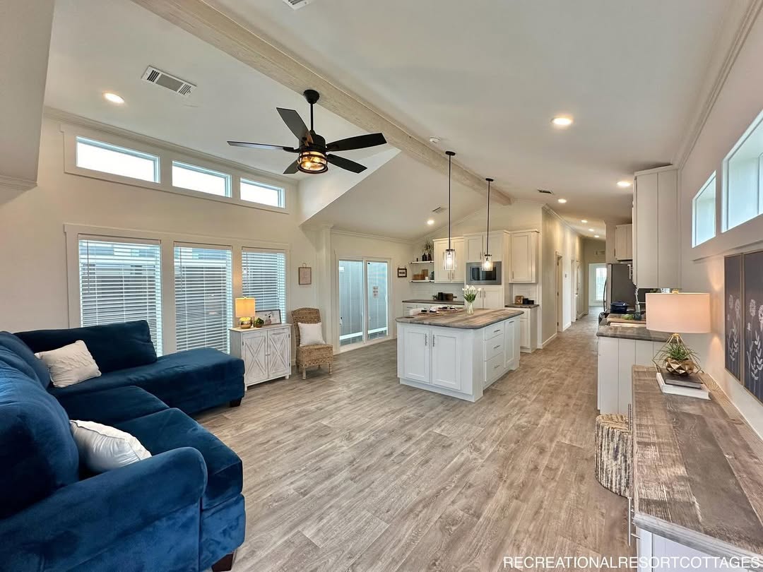 This comprehensive collection of premium tiny homes, park models, and manufactured homes highlights the "Boujee XL" aesthetic, blending modern farmhouse charm with rustic luxury. Exterior architectural styles feature crisp white and cream board-and-batten siding with white metal roofs, black-pillared gabled porches, and elegant black metal railings, as well as a rustic log-cabin style model featuring natural wood siding and a forest green metal roof. Interiors emphasize an upscale lifestyle with vaulted ceilings, exposed wood beams, and white shiplap walls. Gourmet kitchen designs range from rustic wood cabinetry with stone-look backsplashes to sophisticated modern spaces with white or grey cabinetry, marble-look countertops, stainless steel farmhouse sinks, and distressed wood islands. Functional luxury is integrated throughout open-concept living areas, featuring wide-plank wood-look flooring, industrial-style ceiling fans, and large windows or transom glass that provide abundant natural light. Many models also include integrated lofted sleeping quarters accessed by wooden ladders and modern bathrooms with walk-in tile showers.