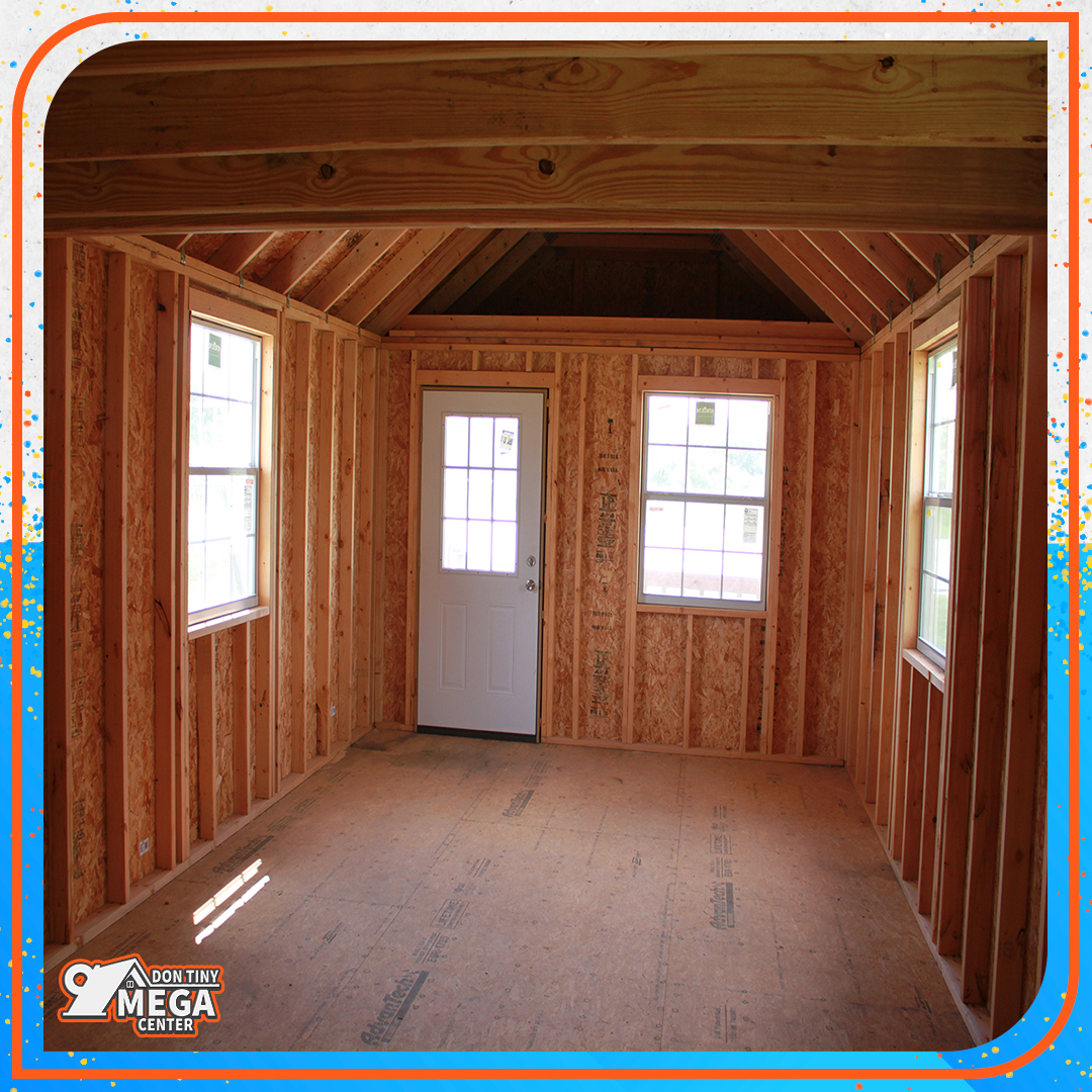 Interior of a small, unfinished wooden cabin with exposed framing. Features three windows and a white door, creating a rustic, inviting atmosphere.