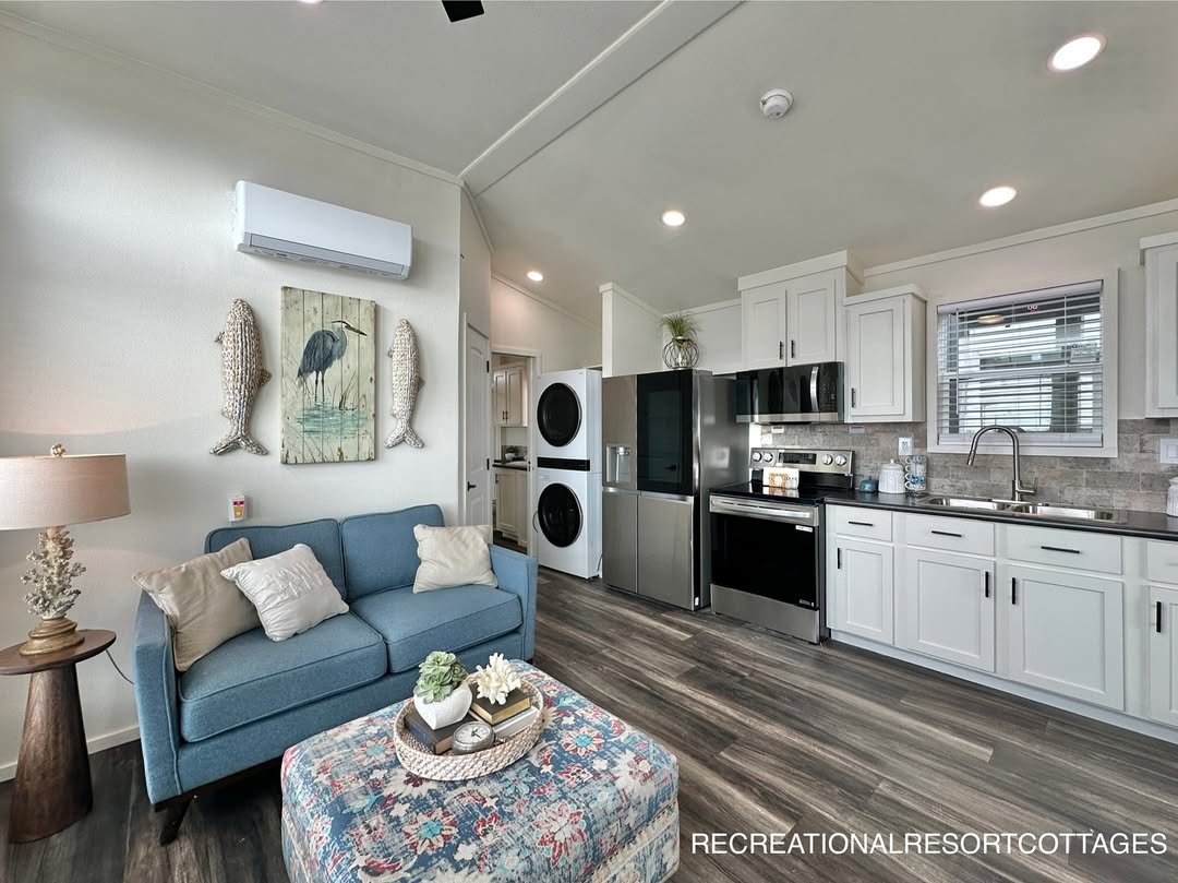 Modern compact living space with a cozy blue sofa, floral ottoman, and large stainless steel appliances. Bright, airy, and neatly arranged kitchen.