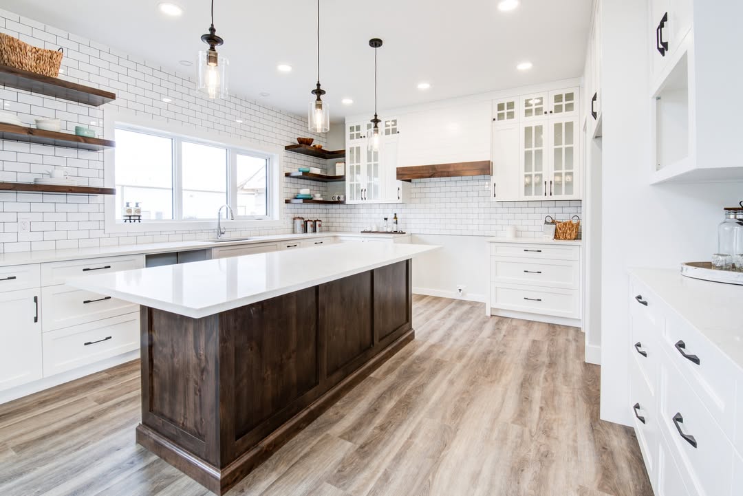 Bright, modern kitchen with a central dark wood island, white cabinets, and wood shelves. Features pendant lights, white subway tiles, and wooden floor.