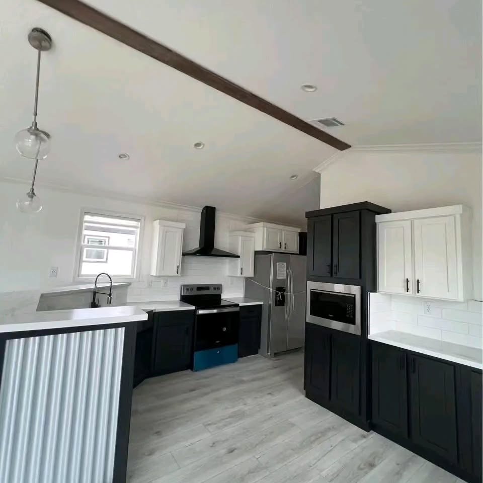Modern kitchen with dark and white cabinetry, stainless steel appliances, and light wood flooring. Pendant lights and white countertops create a sleek look.