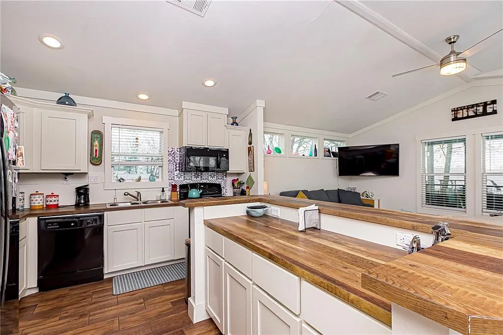 Bright kitchen with wooden countertops, white cabinets, and modern appliances. Ceiling fan and large TV in an adjoining living area, creating a cozy atmosphere.