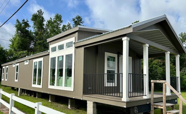 Modern prefab home with a gray facade, large windows, and a small porch, set on a green lawn with trees. The sky is partly cloudy, conveying a serene atmosphere.