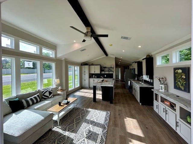 Modern living room with high ceilings, large windows, and light wooden floors. Features a gray sectional sofa, patterned rug, and open kitchen with black and white cabinetry. Bright and spacious ambiance.