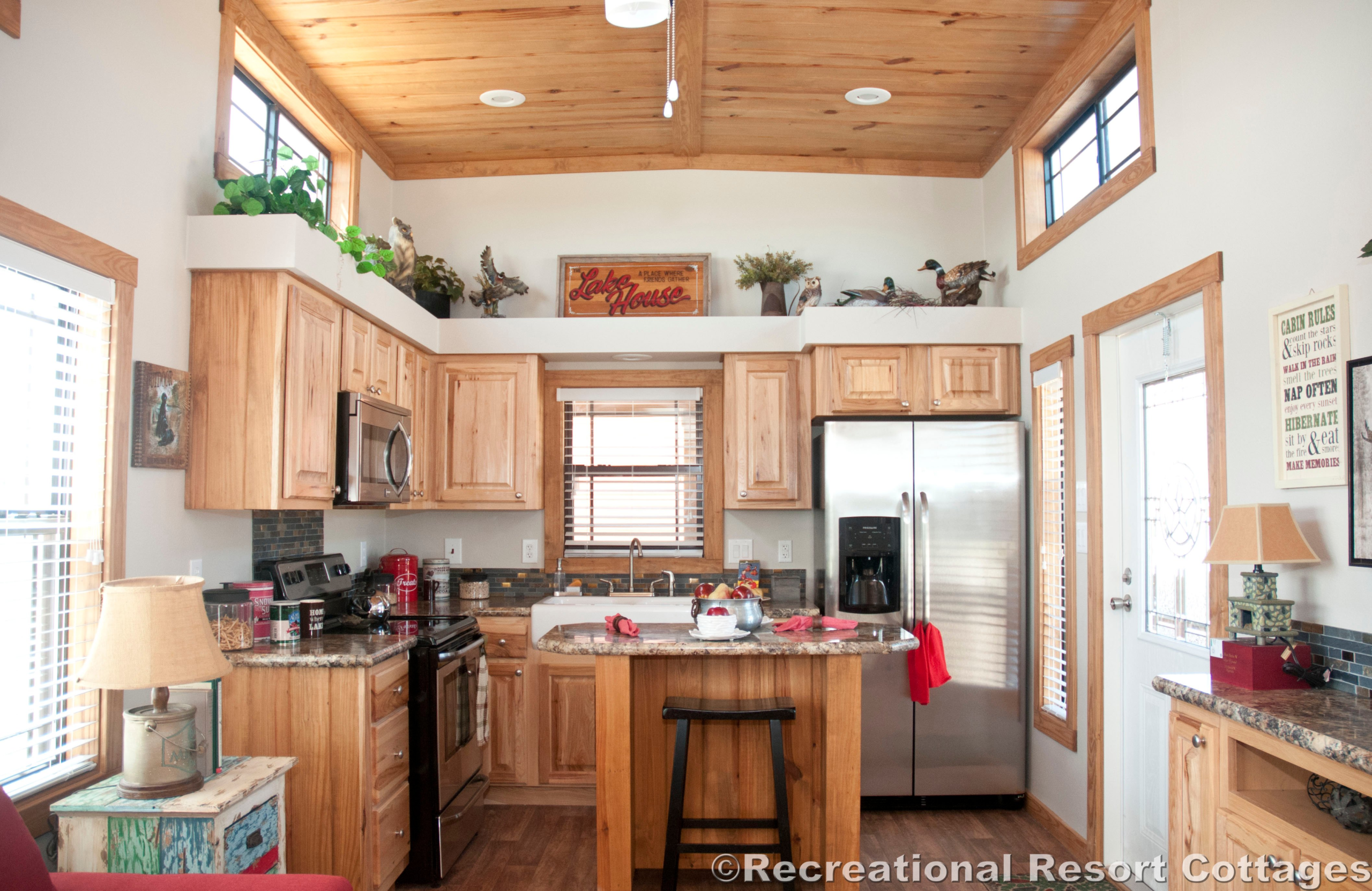 Cozy kitchen with wooden cabinets and ceiling, featuring stainless steel appliances, a central island, and large windows. Rustic and inviting.