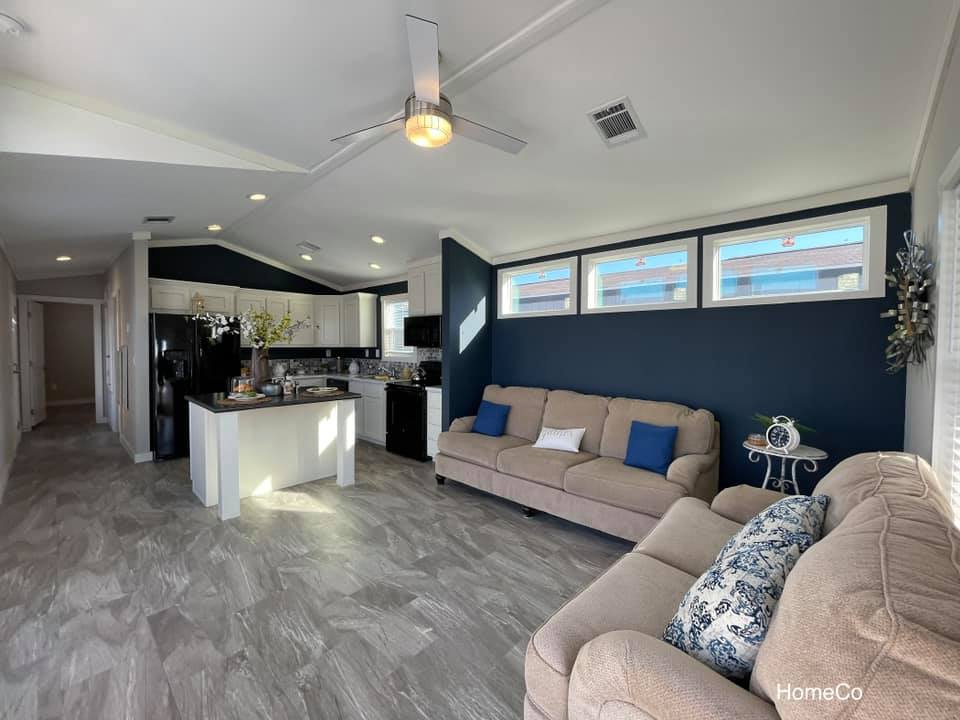 Modern open-concept living room and kitchen with gray tiled floors and navy accent wall. Beige sofas with blue cushions create a cozy atmosphere.