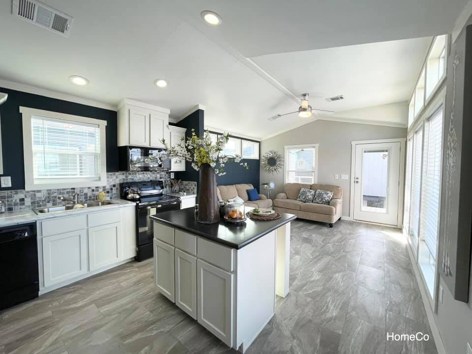Modern open-plan kitchen and living area with white cabinetry and black countertops. Neutral tones and natural light create a cozy, inviting atmosphere.