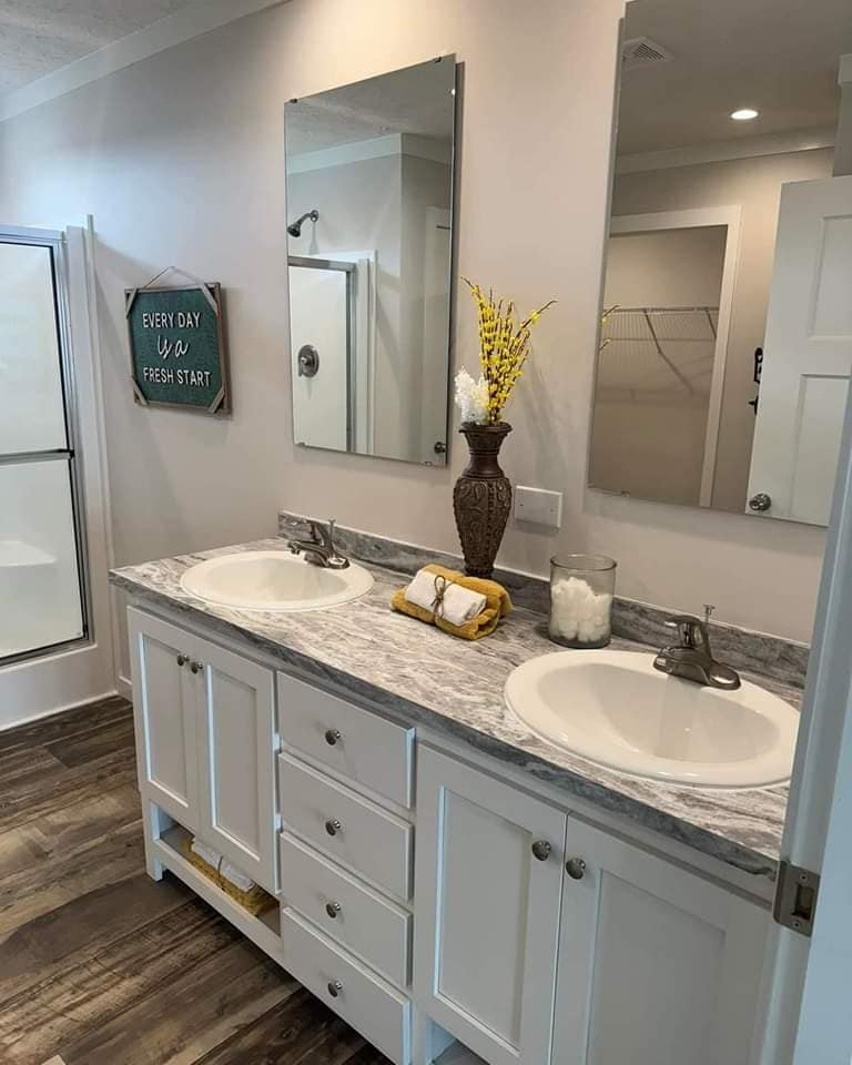 Elegant bathroom with double sinks, gray marble countertop, and decorative vase with yellow flowers. Mirrors above sinks, sign reads "Every day is a fresh start."
