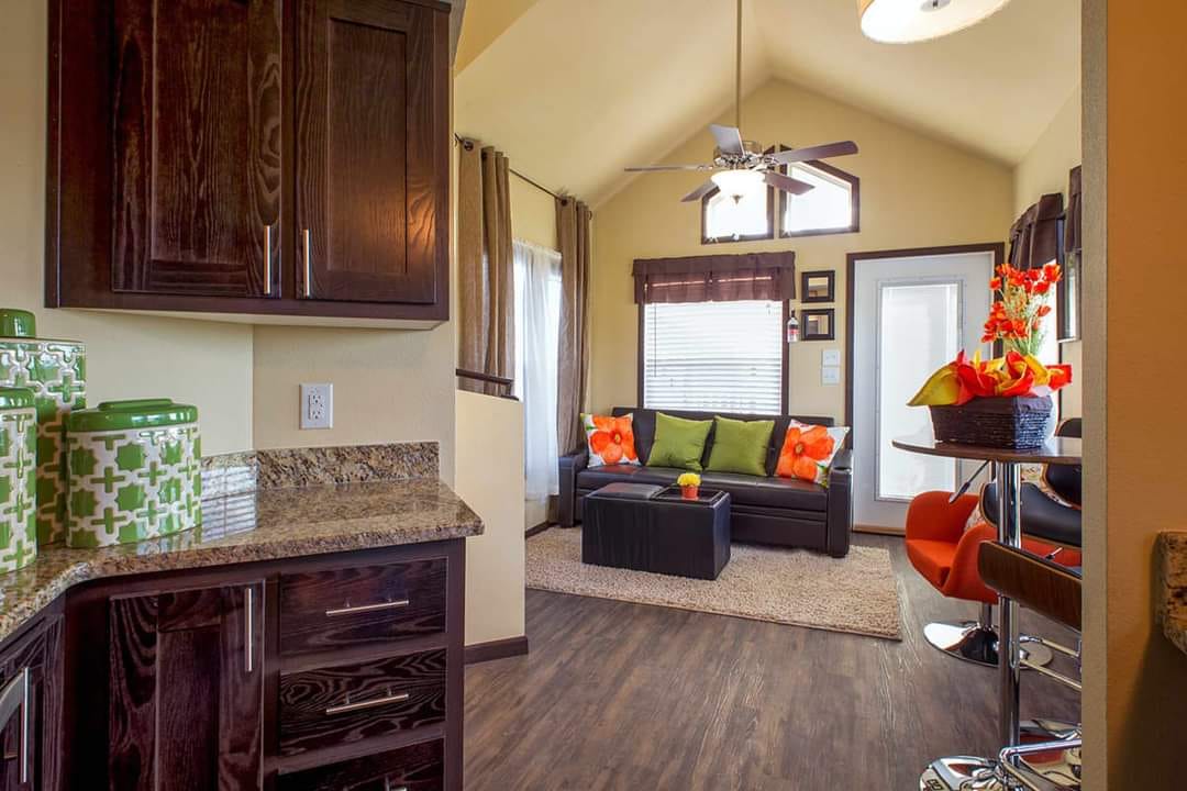 Cozy living space with wooden cabinets, green and orange accents, and a small sofa. Warm, inviting tones and modern decor create a welcoming vibe.