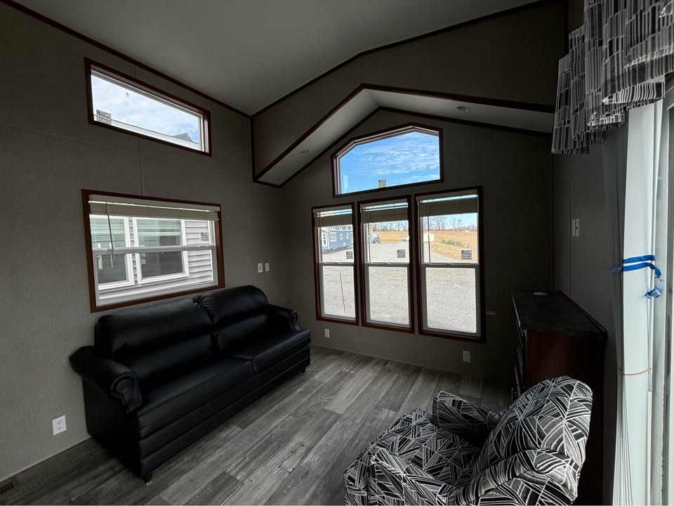 Cozy living room with a black leather sofa against a gray wall, geometric-patterned armchair, large windows showcasing a bright, outdoor scene.