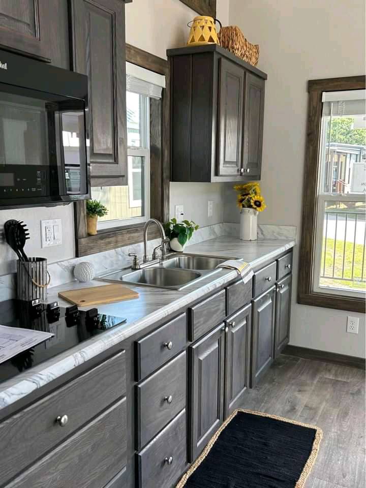 Cozy kitchen with dark wood cabinets and marble countertops. A sink, induction cooktop, and sunflowers in a vase add a warm, welcoming touch.