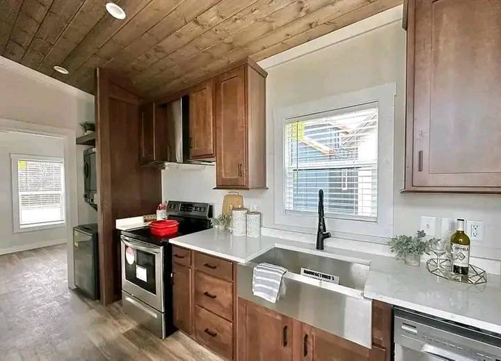Modern kitchen with dark wood cabinets, stainless steel appliances, and farmhouse sink. A bright window, wooden ceiling, and cozy, inviting feel.