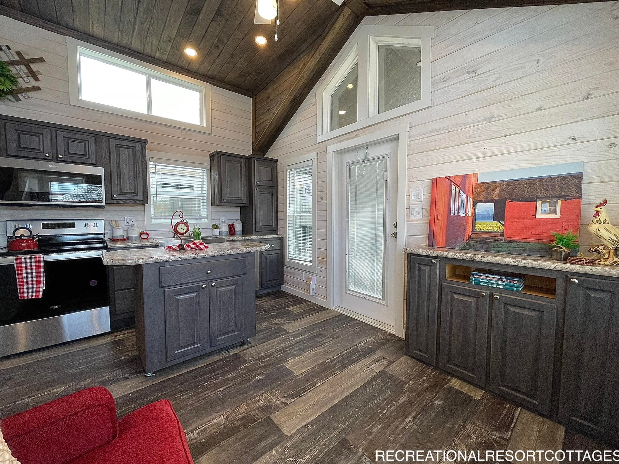 Cozy kitchen interior with dark wood cabinets, stainless steel appliances, and a high ceiling. A painting and rooster figurine add warmth and character.