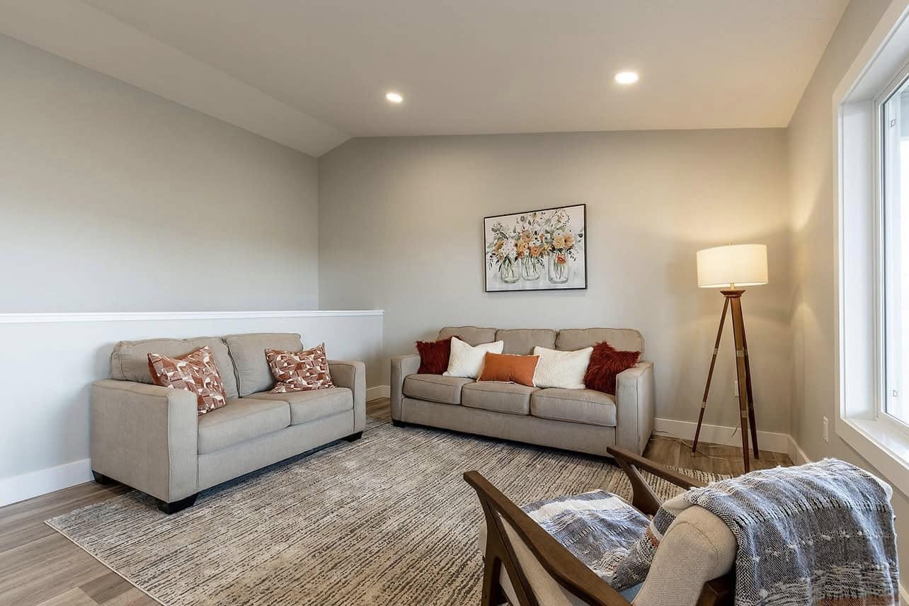 Cozy living room with beige sofas and assorted cushions, a large rug, and a modern floor lamp. Wall art of flowers enhances the warm, inviting ambiance.