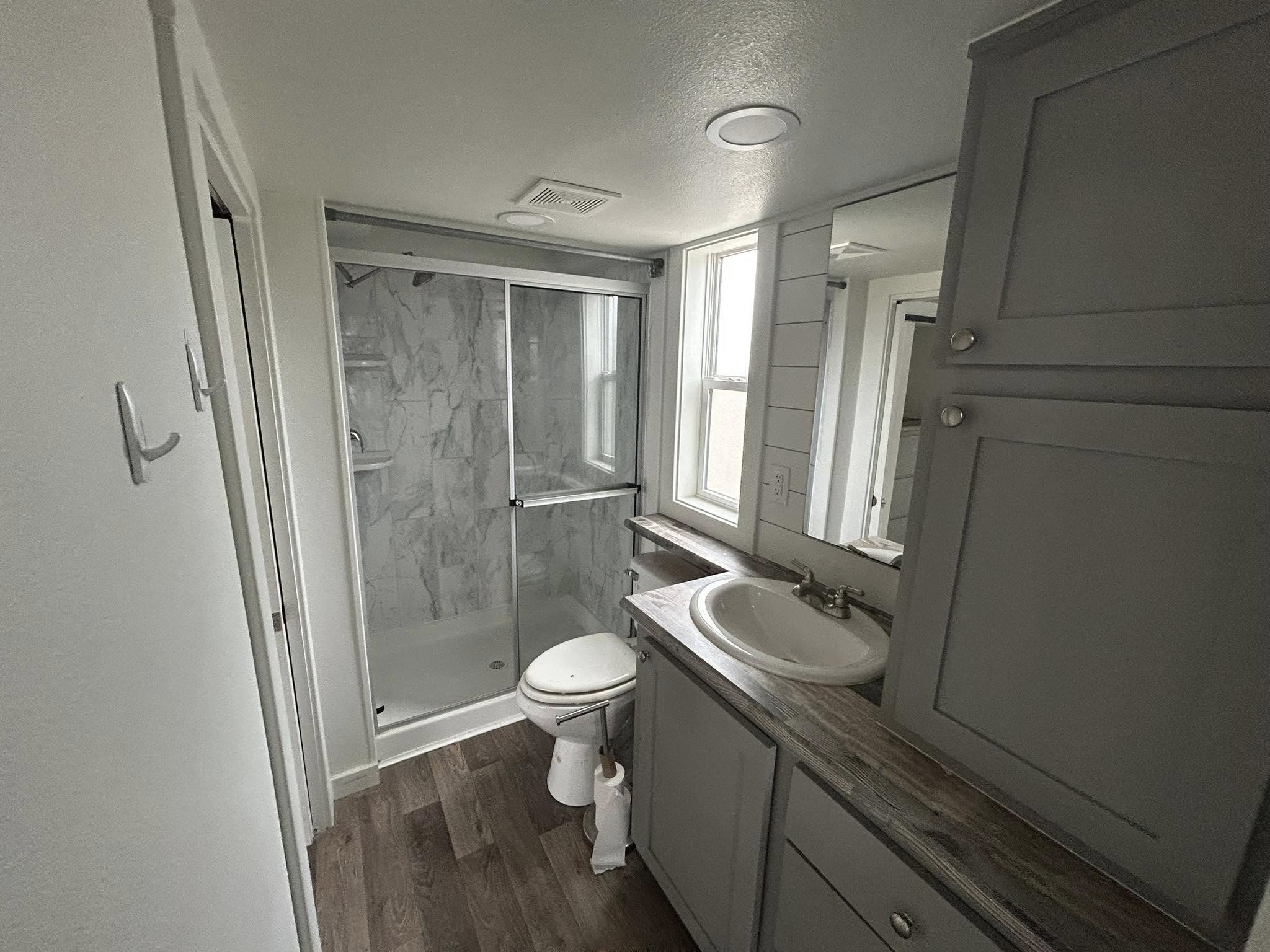 Modern luxury tiny home interior featuring a bright open-concept living area with a grey tufted sofa, a geometric monochromatic area rug, and a rustic kitchen island with a reclaimed wood countertop, showcasing a space-saving loft with a black metal safety railing and a sleek grey shaker-style kitchen with a farmhouse sink and black appliances under a vaulted white shiplap ceiling for a sophisticated move-in ready turn-key residential design.