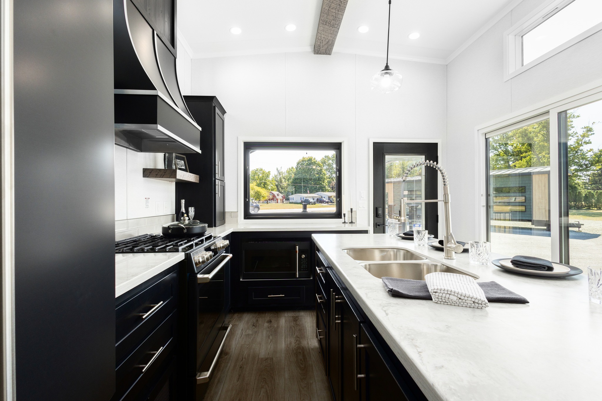 Modern kitchen with dark cabinets and light countertops. Features a large window with outdoor view, stainless steel appliances, and sleek design. Bright, airy feel.