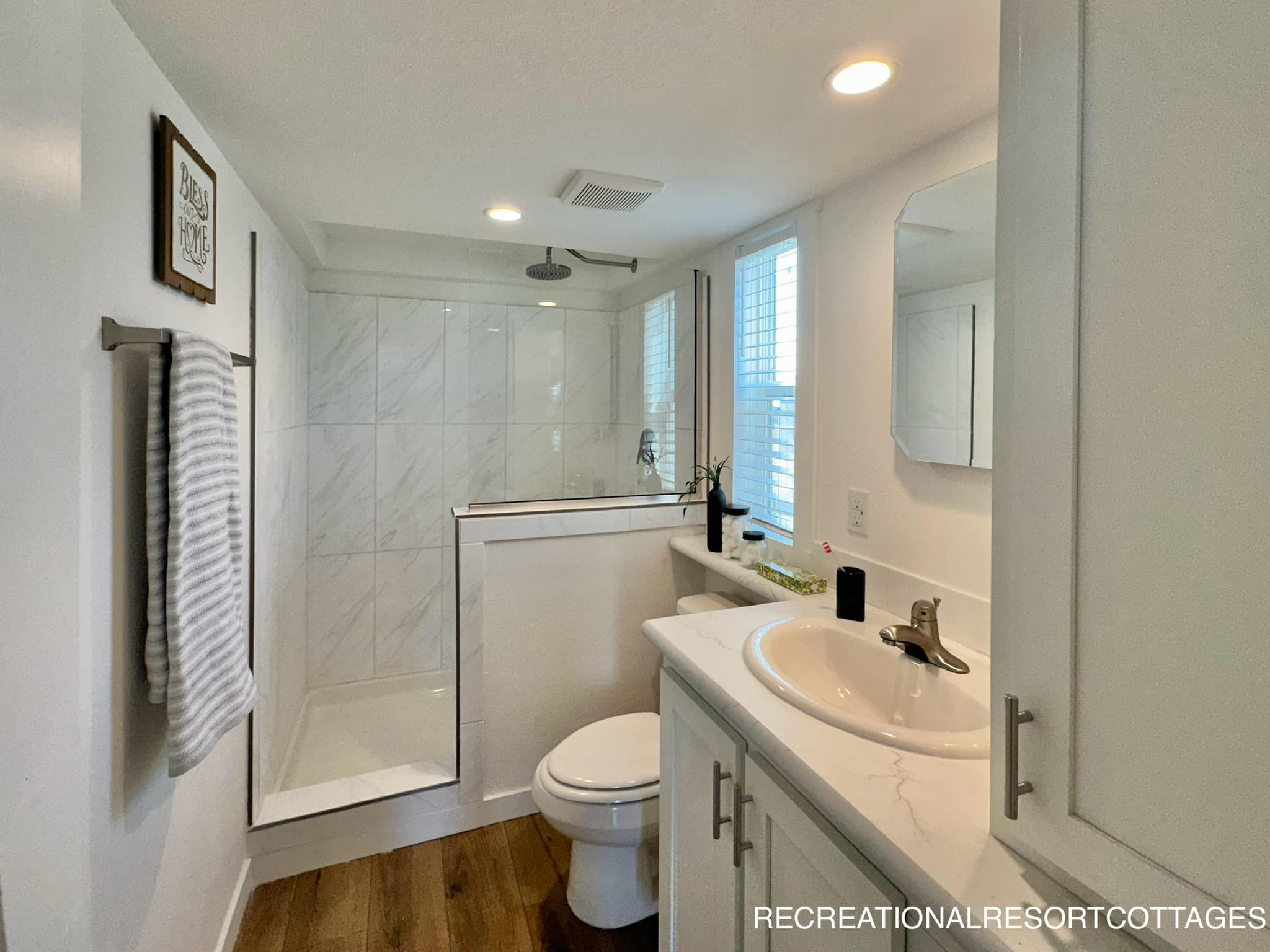 Modern bathroom with a marble-tiled shower, glass door, and overhead rain shower. White countertop with a sink, mirror, and window, creating a fresh, airy feel.