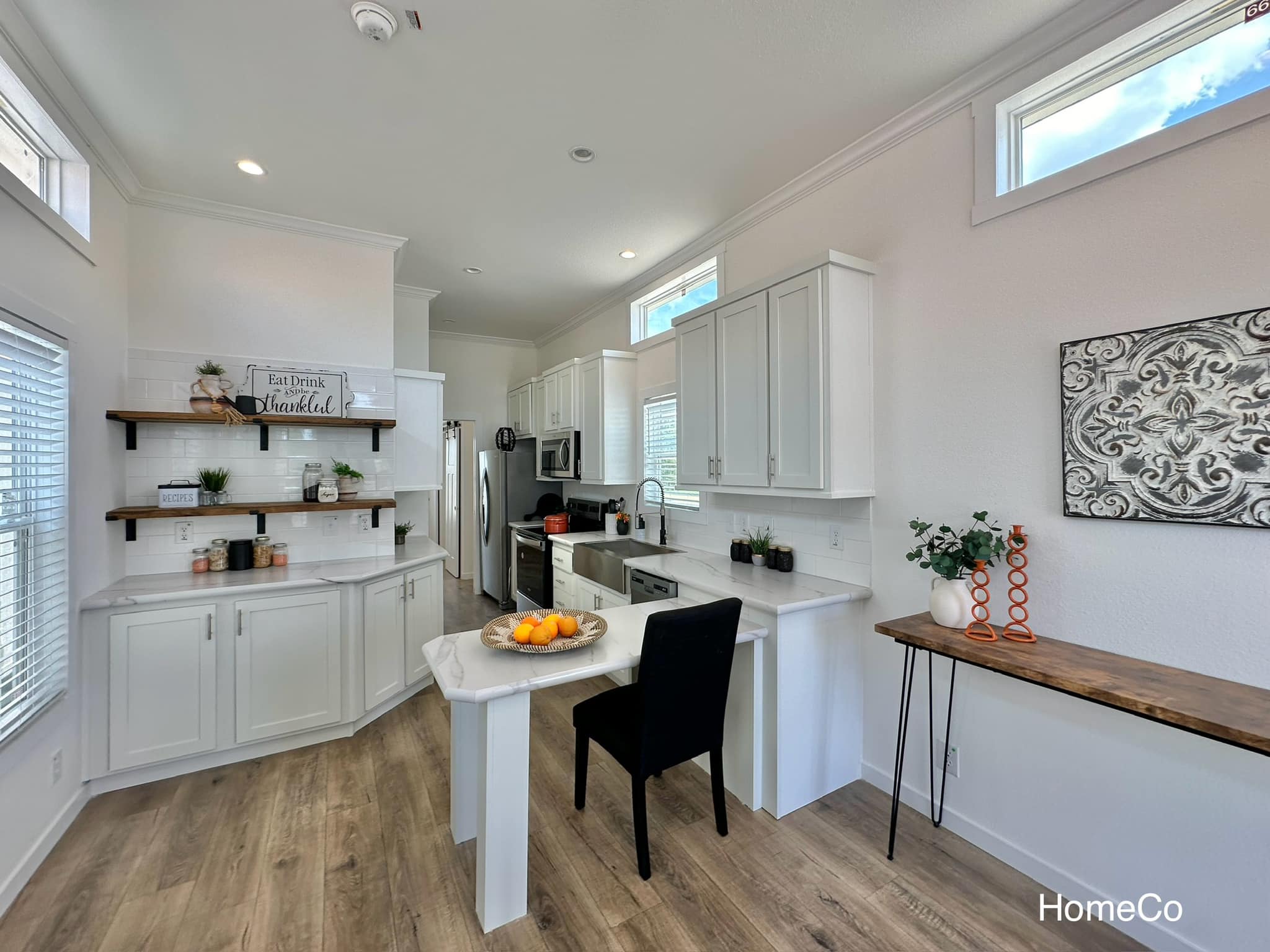 Bright, modern kitchen with white cabinets, stainless steel appliances, and wood accents. A cozy dining area with a black chair and fruit centerpiece adds warmth.