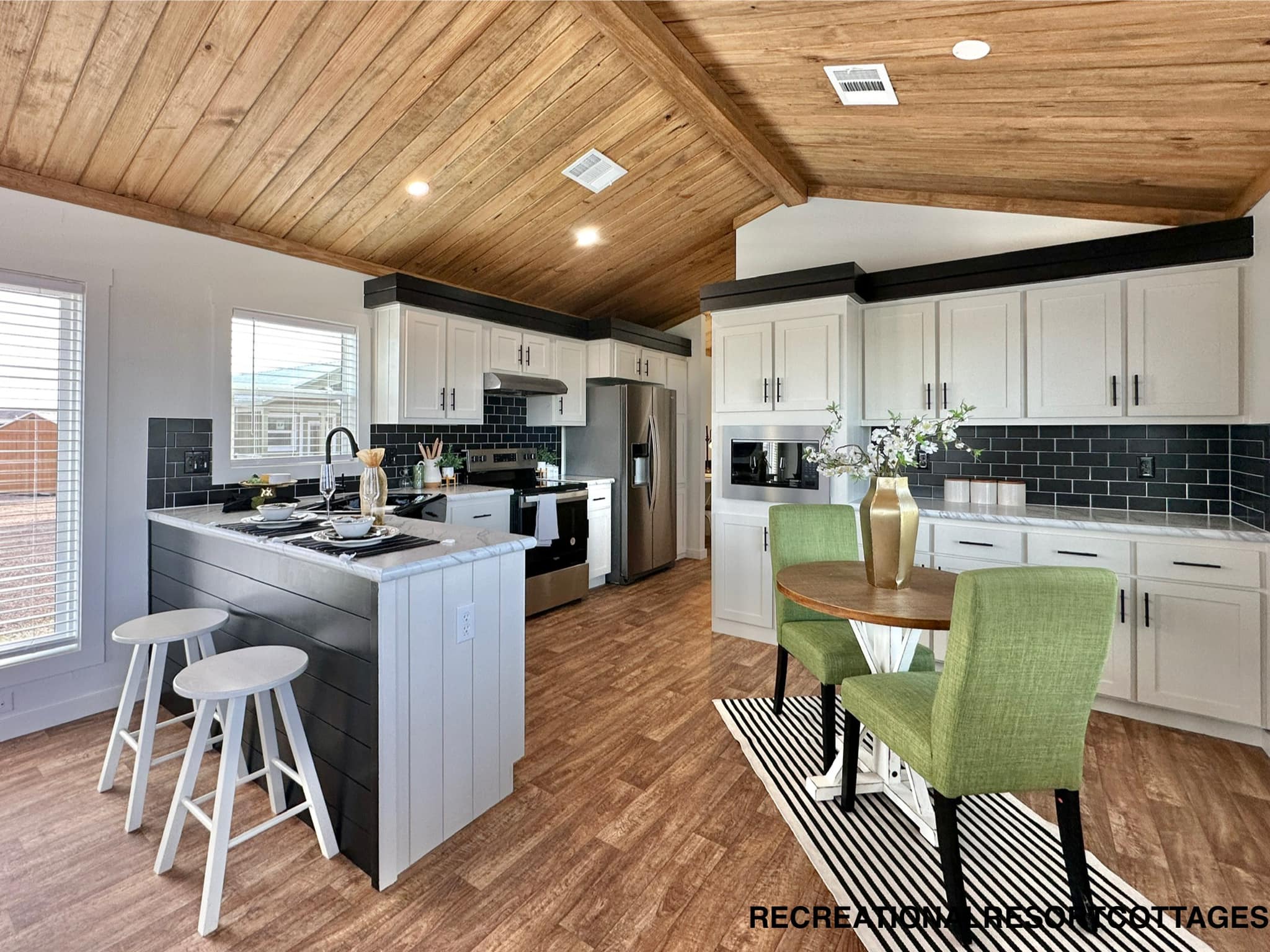 Modern kitchen with wood ceiling, black and white cabinetry, and a central island. Includes green chairs, a round table, and elegant decor, creating a cozy and upscale feel.