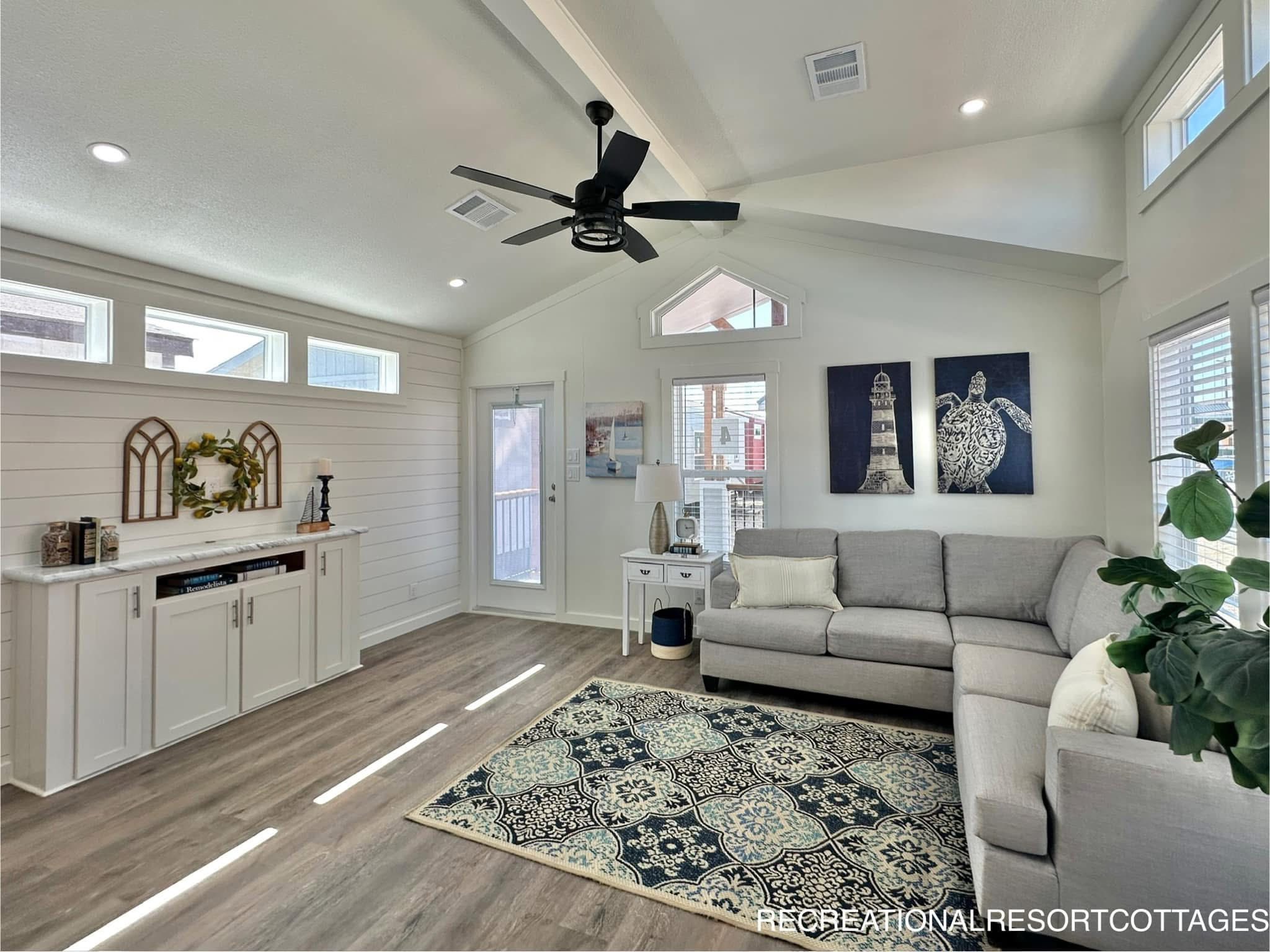 Modern living room with a light gray sectional sofa, navy and white patterned rug, and shiplap walls. Decor includes lighthouse artwork and greenery.