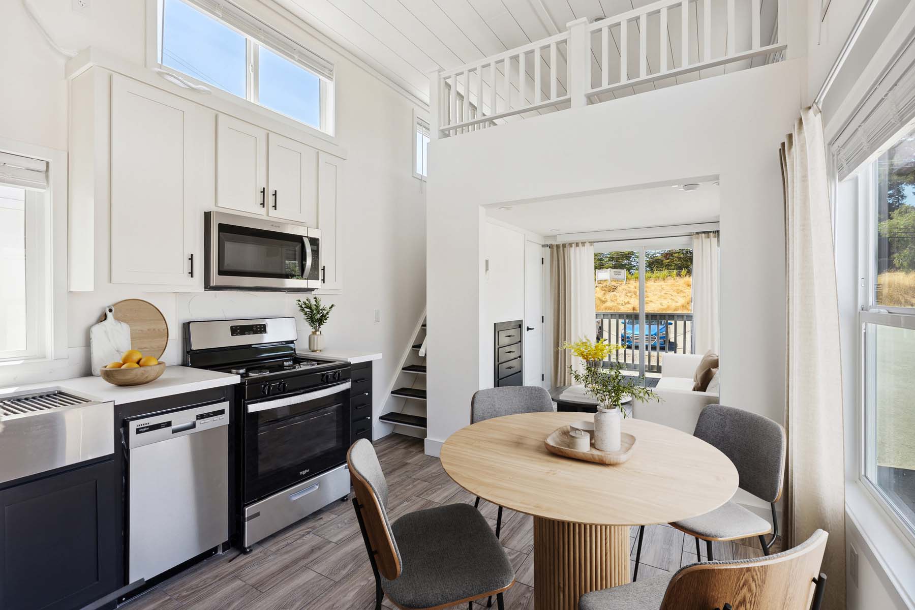 Luxury modern farmhouse park model tiny house on wheels featuring a dual-tone charcoal and white board and batten exterior with a spacious covered front porch, paired with a bright open-concept interior showcasing vaulted shiplap ceilings, a contemporary kitchen with a grey center island and stainless steel appliances, and a cozy living area with a built-in fireplace and large windows for maximum natural light.