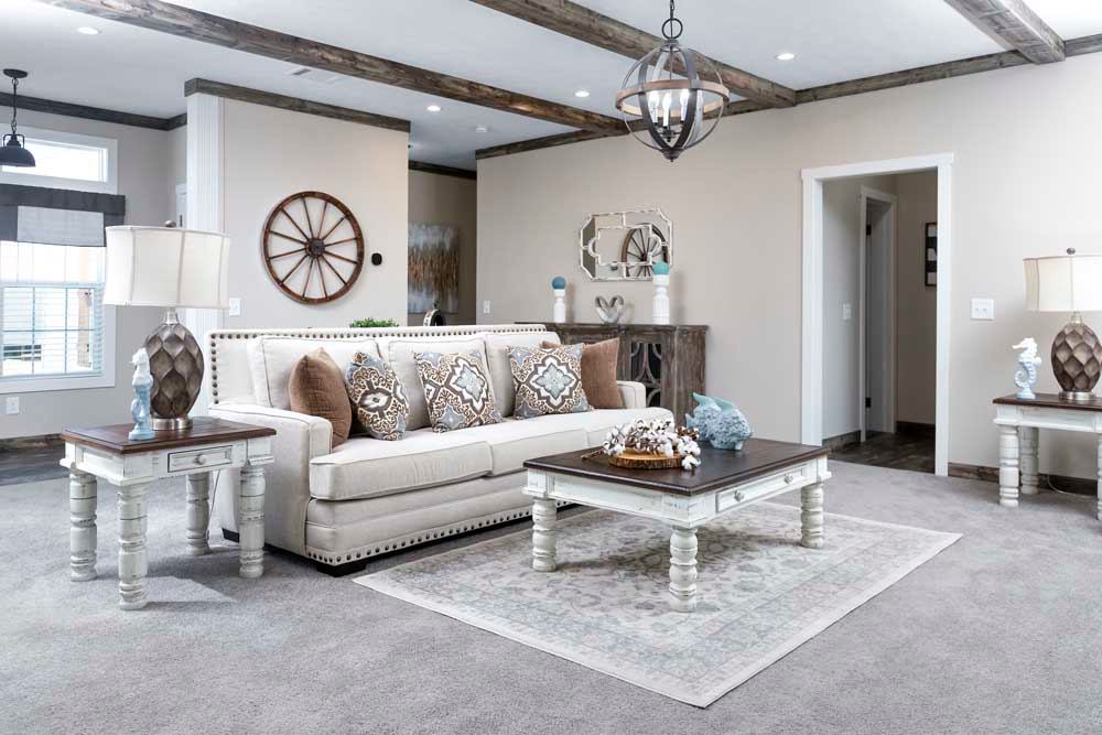 A cozy living room with a beige sofa, patterned cushions, and rustic coffee table. Features wooden ceiling beams, decorative lamps, and soft lighting.