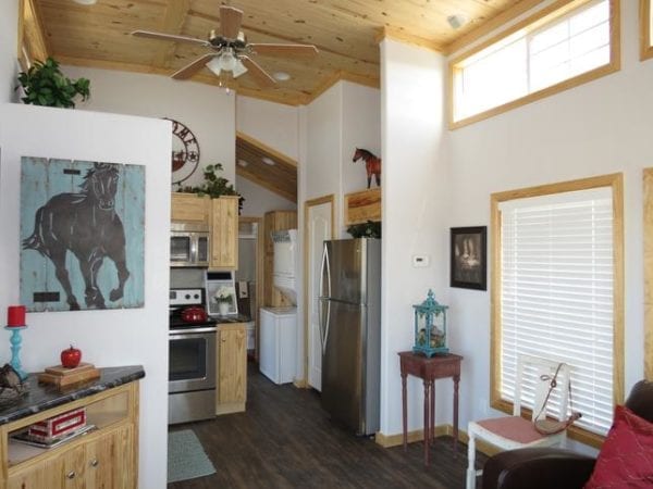 Warm and cozy kitchen with wooden cabinets and stainless steel appliances. A horse painting decorates the wall, and a ceiling fan hangs from the wood-paneled ceiling.