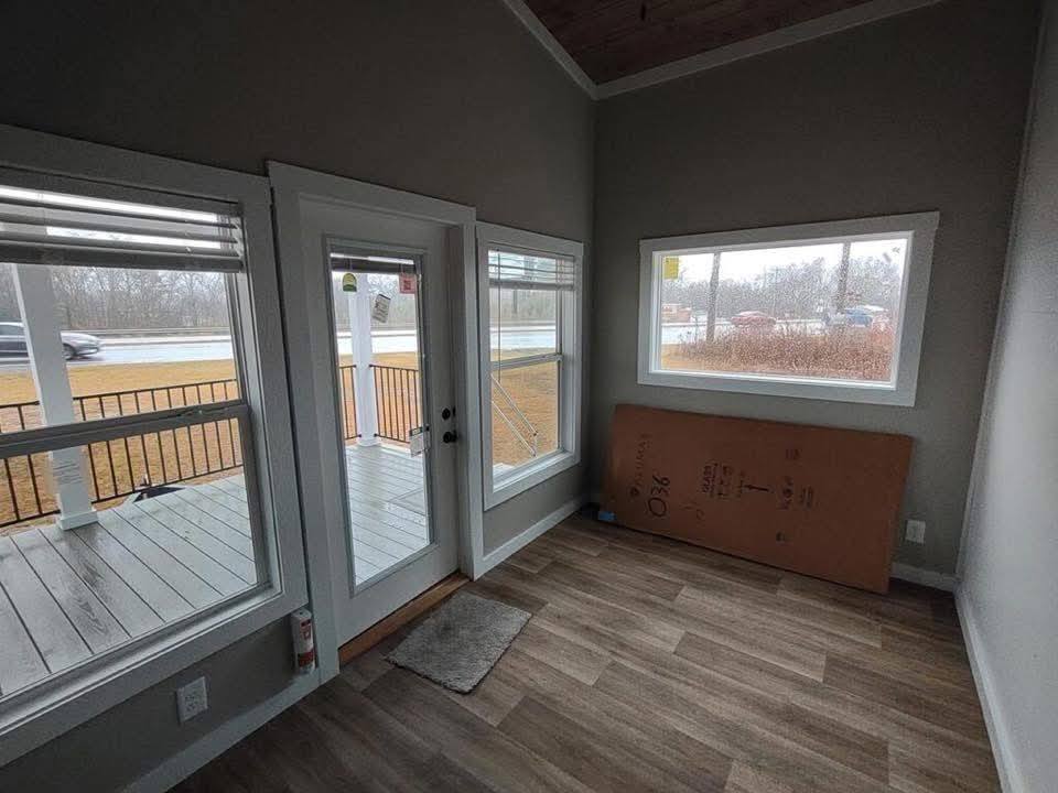 
Gemini said
Modern small home interior entryway featuring durable wood-look vinyl plank flooring, grey walls with crisp white trim, and a glass-paneled front door leading to a covered porch with black metal railings, alongside large energy-efficient windows that fill the compact living space with natural light for a bright and airy 560 sq ft tiny house design.