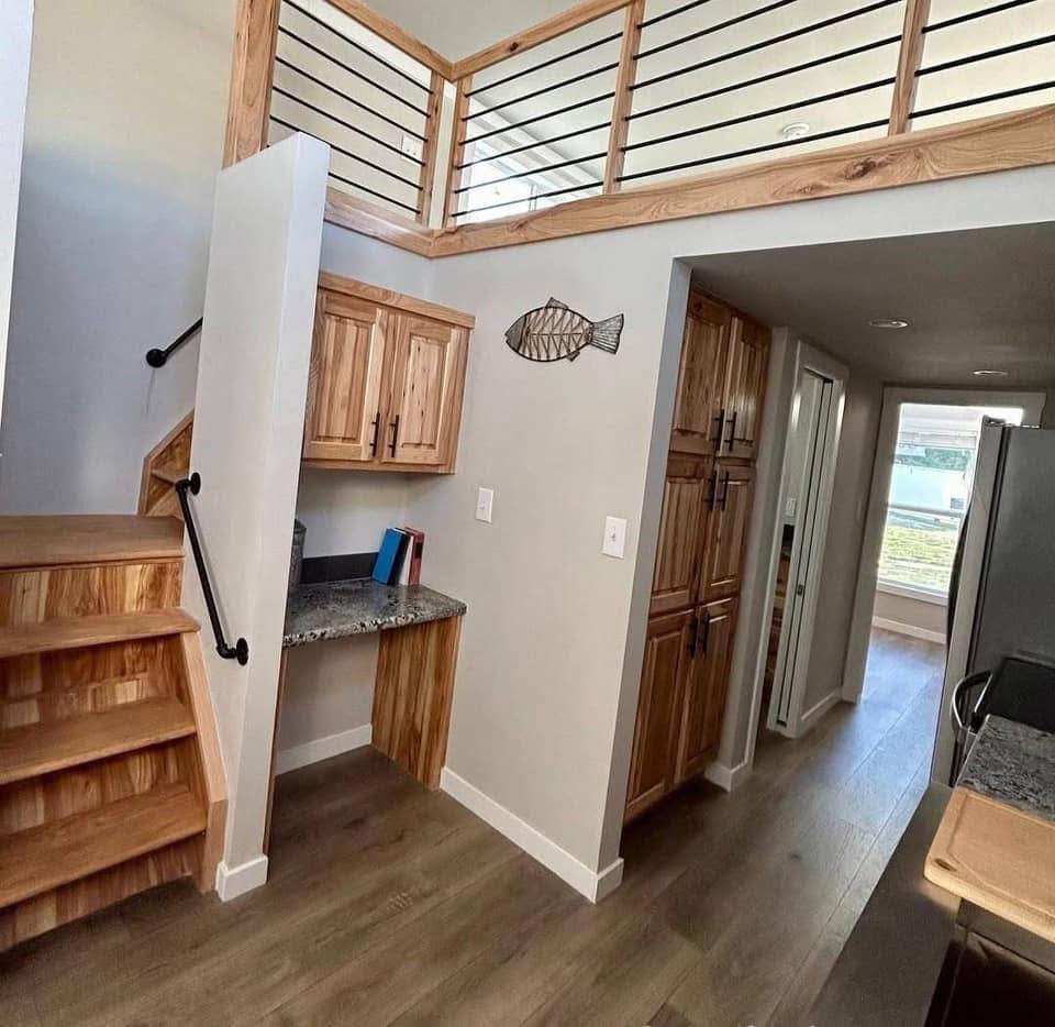 Modern luxury tiny home interior featuring a compact multi-functional living space with a natural wood staircase leading to a loft, built-in wooden cabinetry, a granite-topped workstation, and premium wood-look flooring, all designed with a high-end rustic aesthetic for a sophisticated move-in ready turn-key residential property.