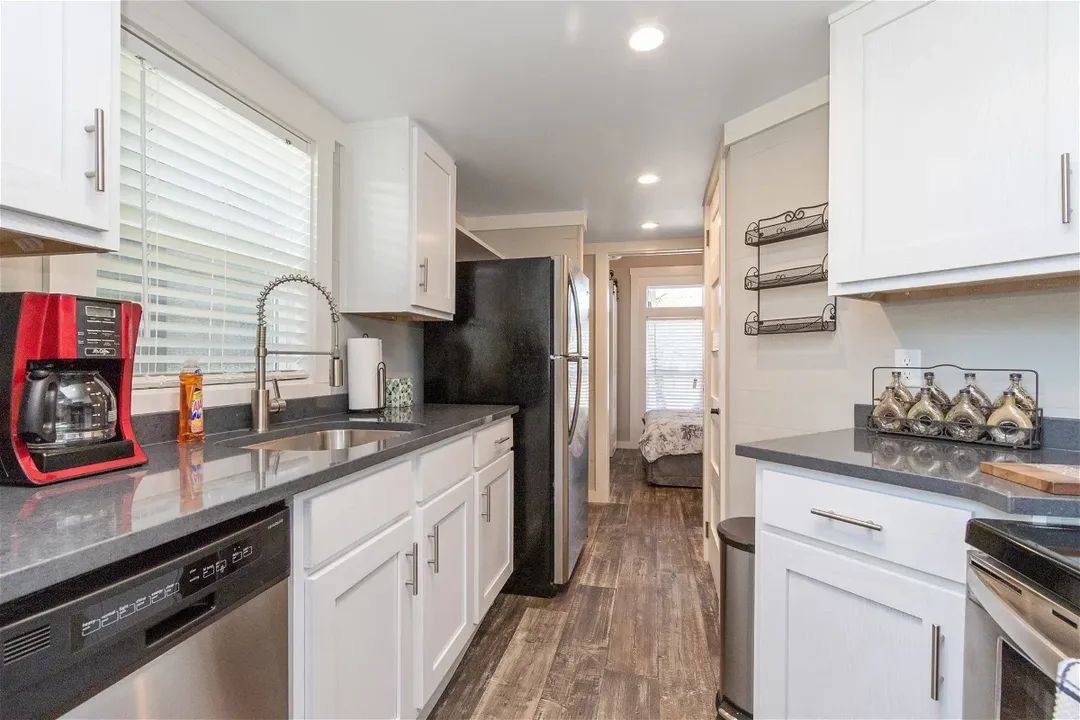 Modern kitchen with white cabinets, dark countertops, and stainless steel appliances. A red coffee maker and decor add warmth. Clean and inviting.