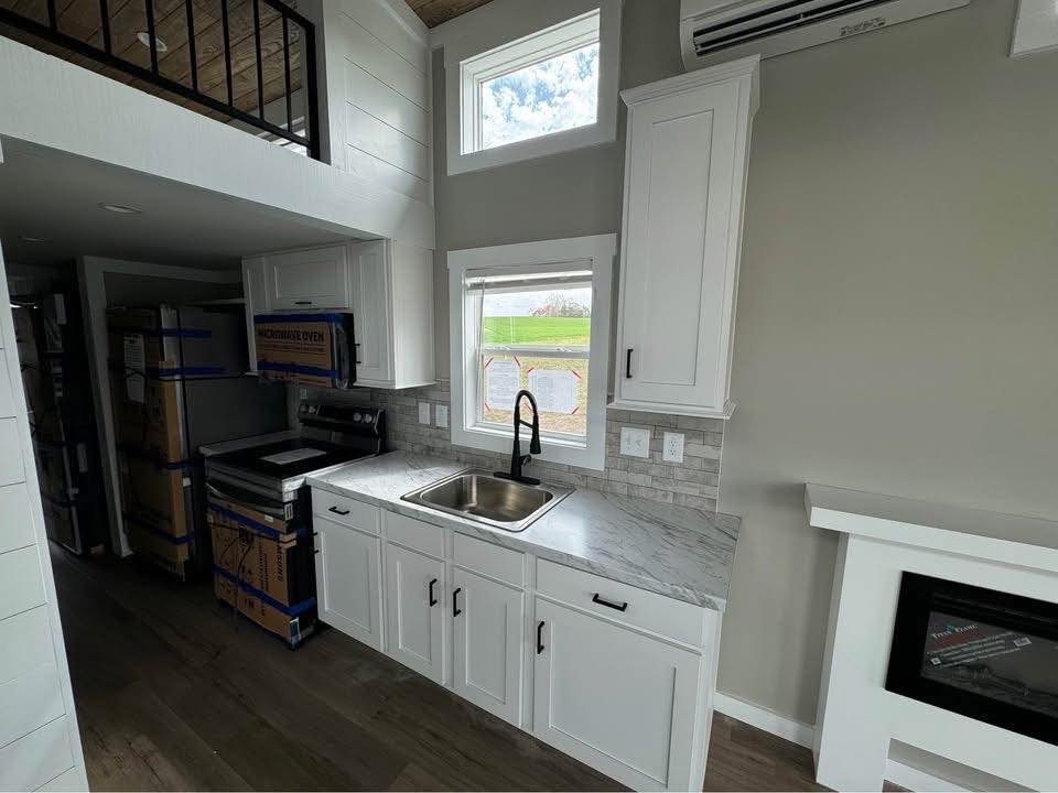 Modern kitchen with white cabinets, marble countertops, and a stainless steel sink. A window above the sink offers a view of green grass.