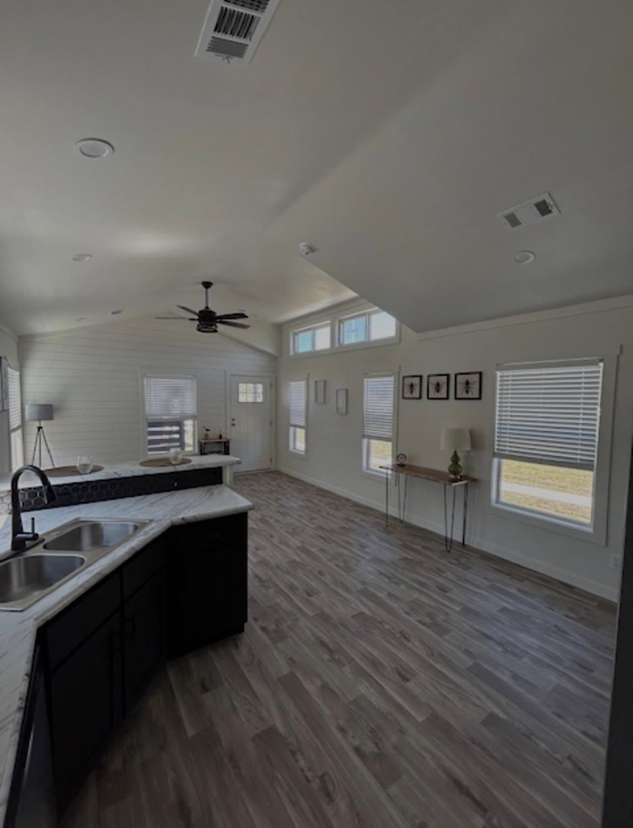 Bright, modern kitchen with dark cabinetry, marble countertops, and a double sink. Open layout with light wood flooring and large windows. Airy and inviting atmosphere.