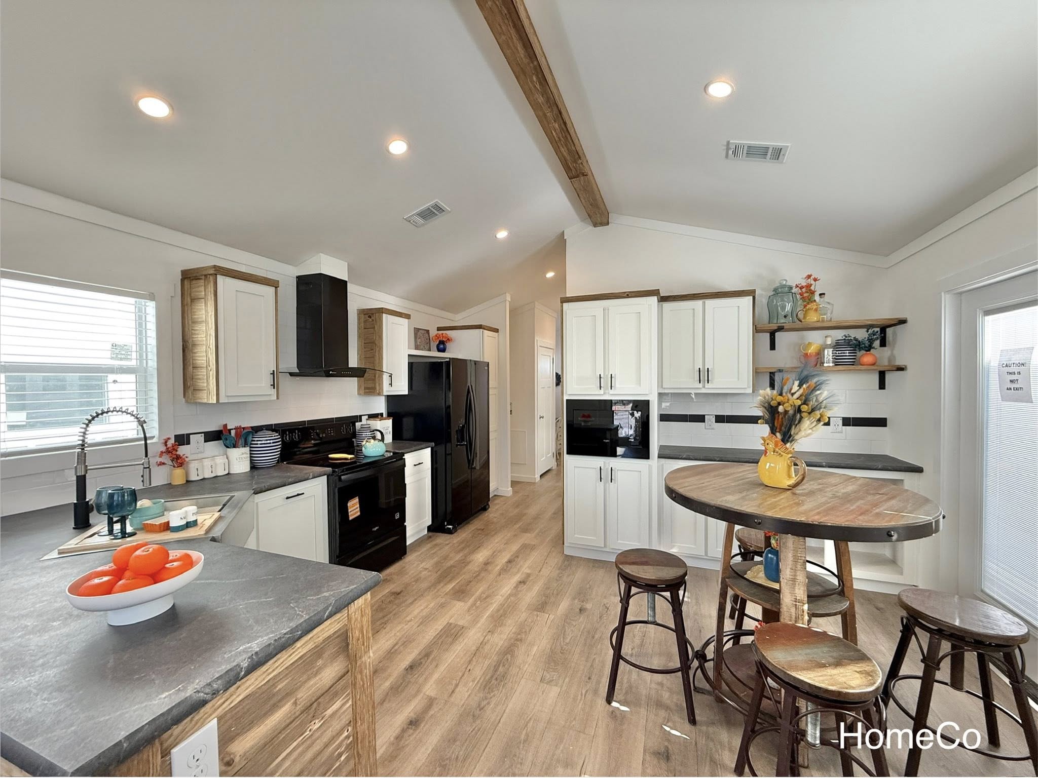Modern kitchen featuring wood floors, a black fridge, stove, and white cabinets. A round table with stools and a bowl of oranges adds warmth.