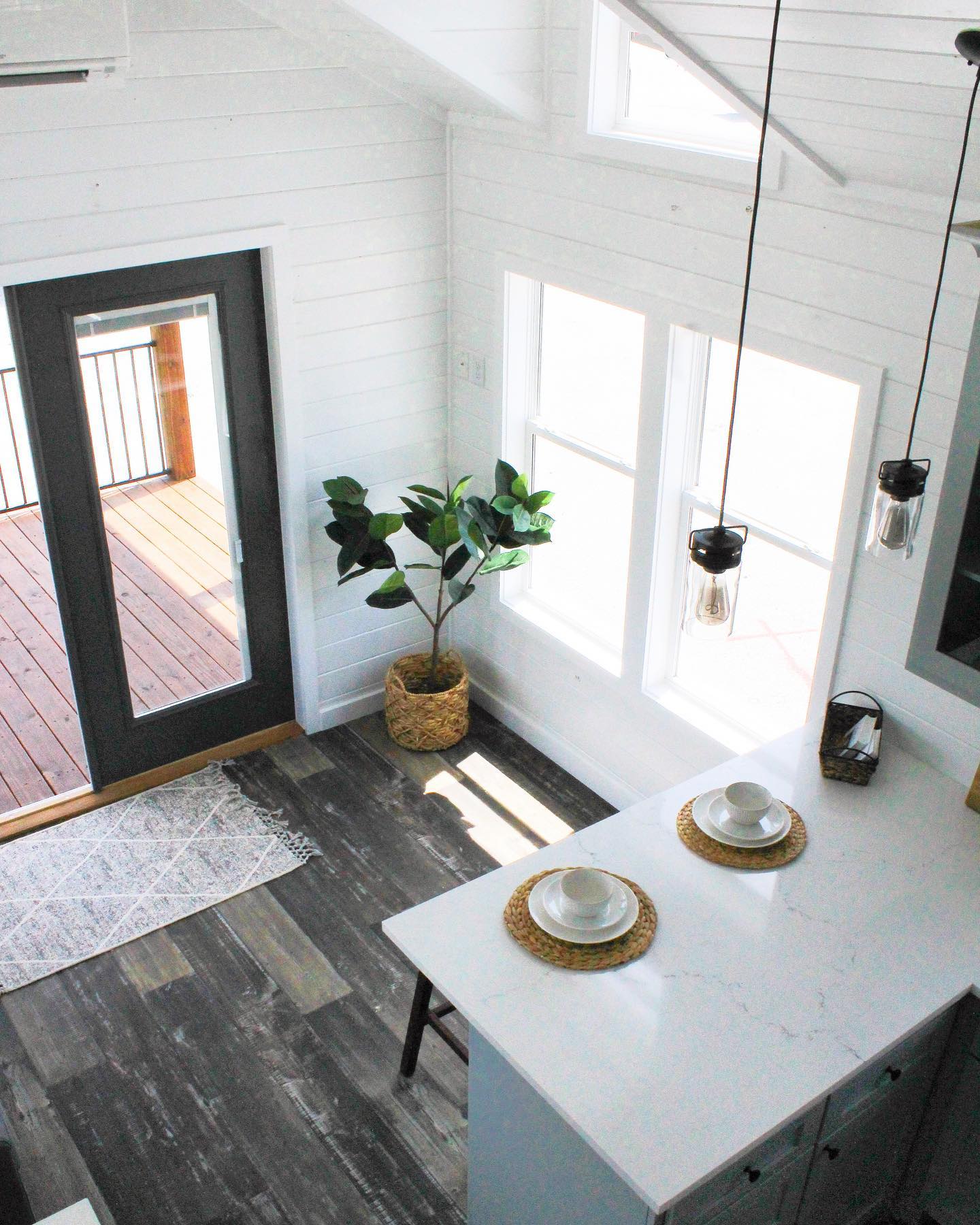 Modern luxury tiny house on wheels featuring a white board and batten exterior with a large covered front porch and metal gabled roof, paired with a bright open-concept interior showcasing vaulted shiplap ceilings, rustic wood beams, a contemporary kitchen with white shaker cabinets, and a cozy living area with a built-in fireplace and large windows for maximum natural light.