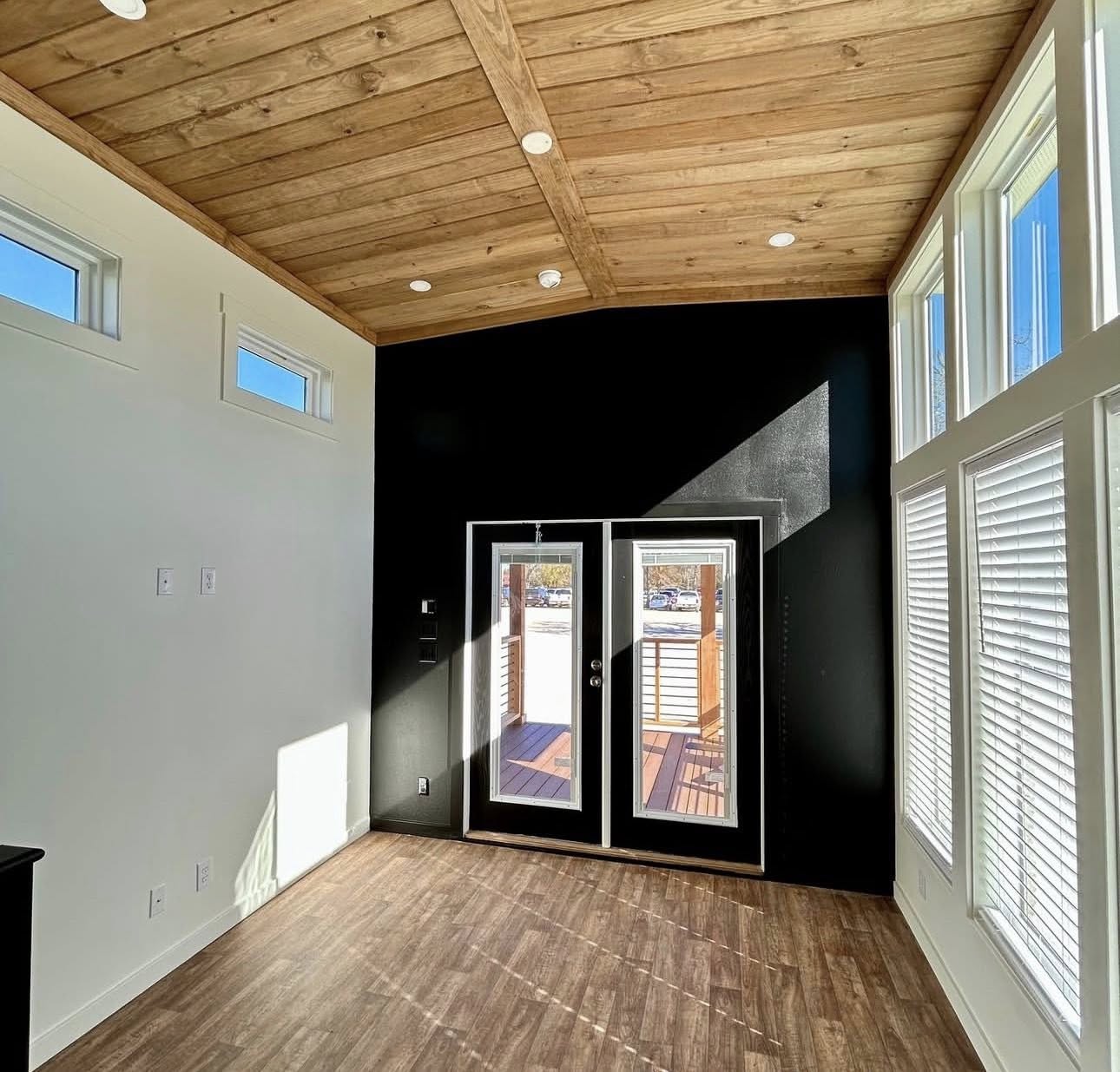 Bright room with wooden ceiling, dark accent wall, and two large glass doors. Sunlight streams through, creating a warm, inviting atmosphere.