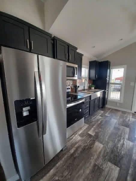Modern kitchen featuring stainless steel appliances, black cabinetry, and wooden flooring. Bright window adds natural light, creating a sleek, inviting space.