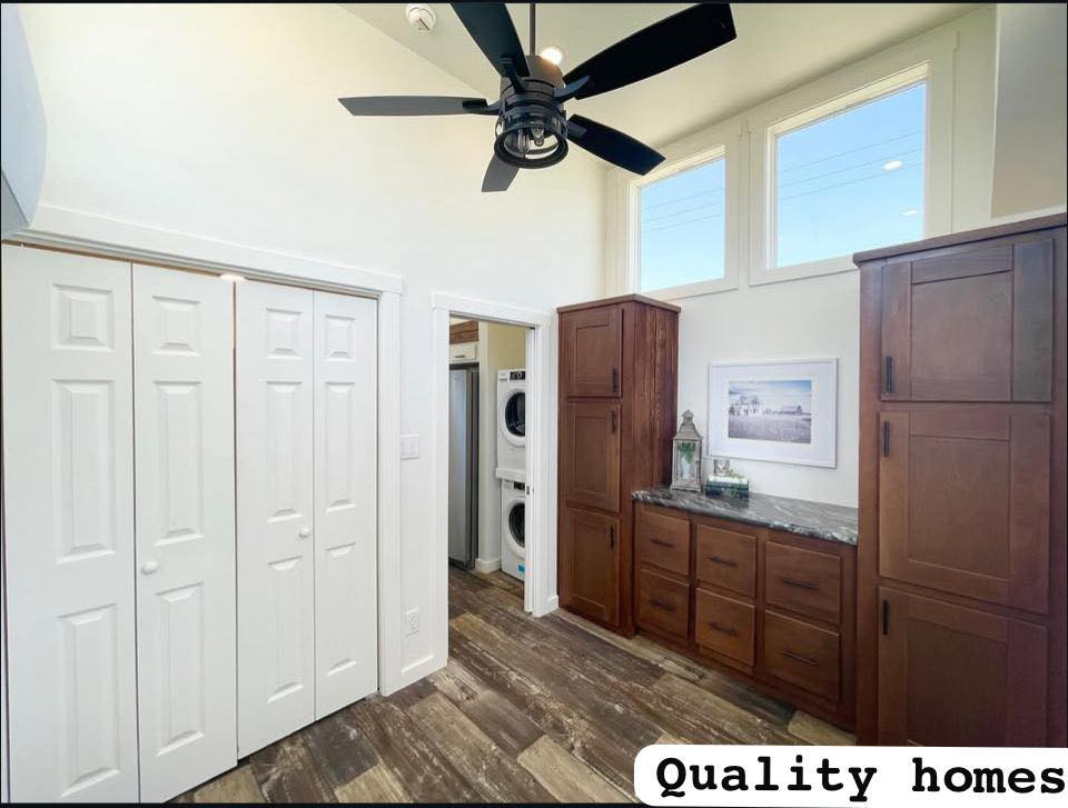 Bright laundry room with wooden cabinets and a stone countertop, housing a washer and dryer. Ceiling fan, large windows; text reads "Quality homes."