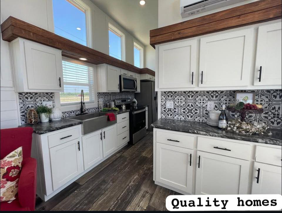 Modern kitchen with white cabinets, black and white patterned backsplash, dark countertops, and wood accents. Bright natural light from tall windows. Cozy atmosphere.