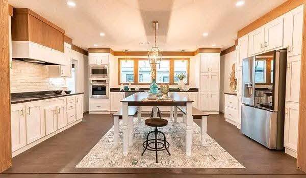 Modern luxury kitchen and open-concept living area featuring white shaker cabinets, a large marble-patterned island with seating, and stainless steel appliances, seamlessly transitioning into a bright dining space with a contemporary wooden table and industrial pendant lighting for a sophisticated turn-key residential home interior.